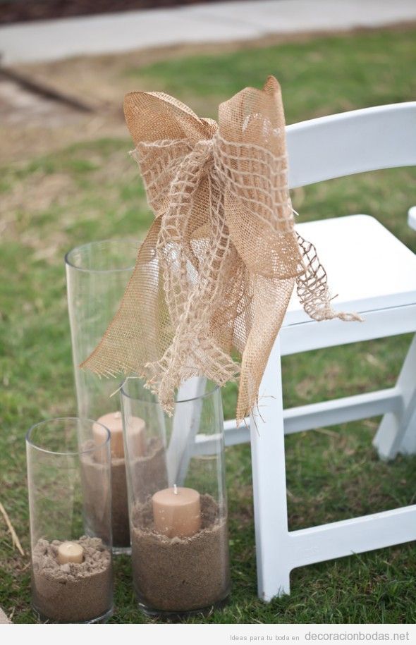 Velas con arena, lazos de yute y sillas blancas para una boda en el jardín