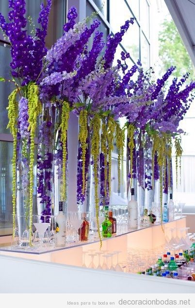 Jarrones altos con flores lilas para decorar una barra de bebidas en una boda