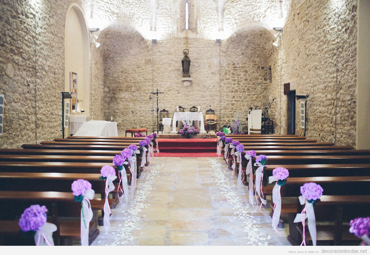Bancos de iglesia con paredes de piedra decorados con flores lilas